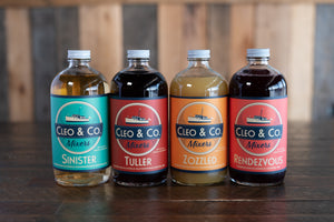 Four Cleo & Co. mixer bottles sit on top of a wooden table | Sinister | Tuller | Zozzled | Rendezvous